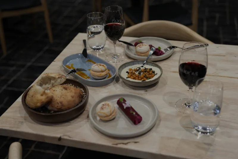 A Rakkas table spread - bread bowl, dips, mezze and red wine in etched glasses