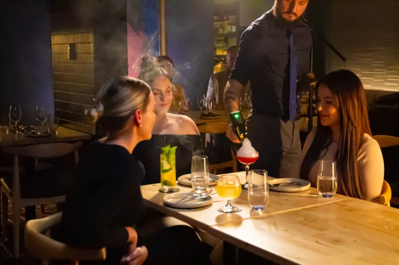 A staff member smoking a cocktail tableside for two guests at Rakkas